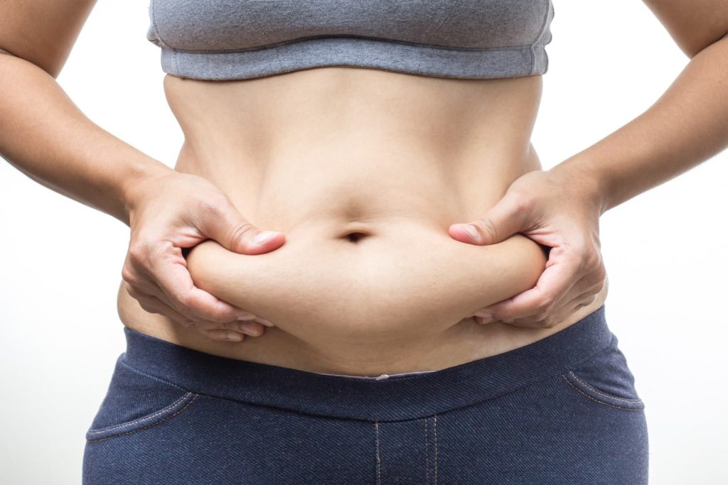Mujer sujetando la grasa acumulada en el abdomen, mostrando grasa localizada resistente a dieta y ejercicio.